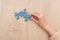 Partial view of female hand with blue puzzles on wooden table.