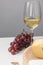 Partial view of maasdam cheese on wooden board, wine glass, almond and grapes on gray