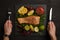 partial view of male hands with cutlery, grilled salmon steak, sauce and arranged citrus fruits on black surface