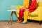 partial view of retro styled women sitting on yellow sofa with aquarium fish on coffee table at colorful apartment, doll