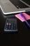 Partial view of a silver keyboard of a laptop with a calculator, and a pink post-it notes with a pencil on a dark wood desk