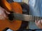 Partial view of a straight hands played wooden trekking guitar, strings swinging, arm laid on to play