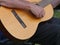 Partial view of a straight played wooden trekking guitar, strings swinging, arm laid on to play