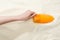 Partial view of woman holding orange sunscreen above golden sand.