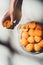 partial view of woman holding piece of apricot with metal tray full of ripe apricots near by on light