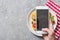 Partial view of woman taking picture of Pappardelle with tomatoes, basil and prosciutto on smartphone on grey surface