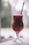 Partially blurred glass of red berry smoothie with straw, on wooden table with white tablecloth near window. Vertical