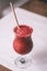 Partially blurred glass of red berry smoothie with straw, on wooden table with white tablecloth. Vertical