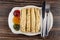 Partitioned dish with jams, pancake rolls, fork and knife on table. Top view