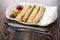 Partitioned dish with jams, pancake rolls, tissue, fork, knife on wooden table