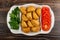 Partitioned dish with patties, parsley, tomato on wooden table. Top view