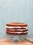 Partly frosted cake on a glass stand, decoration in a process