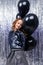 A party. Attractive young stylish caucasian girl stands with black helium balloons on a shiny holiday background.