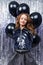 A party. Attractive young stylish caucasian girl stands with black helium balloons on a shiny holiday tinsel background