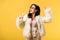 Party girl in faux fur jacket and sunglasses dancing with champagne isolated on yellow