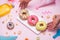 Party. Hand holding plate of colourful sugary round glazed donuts and bottles of drinks on pink background.