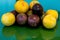Pasiflora fruits and large yellow plums on on green glass table, selective focus