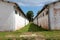 Passage between two long dilapidated white hangars made with red bricks surrounded with uncut grass at abandoned military complex