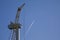 An passenger aircraft is drawing contrails behind a wind turbine under construction