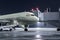 The passenger aircraft stands at the jetway on an airport night apron. The baggage compartment of the airplane is open and the