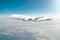 Passenger airplane flying at flight level high in the sky above the clouds and blue toned sky. View directly in front, exactly.