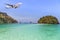 Passenger airplane landing above small island in blue sea and tropical beach