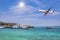 Passenger airplane landing above tropical sea with cruising ships and boats moored in bay.