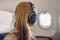 Passenger in airplane using headphones. Woman in plane cabin listening to music on headphones.