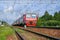 Passenger electric train moves against the background of green trees