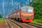 Passenger electric train moves on a background of green forest and dark blue sky