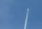 A passenger plane flies in the blue sky leaving a trail of steam behind