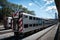 Passenger trains traveling through a bustling train yard with a clear blue sky in the background