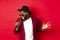 Passionate black male singer performing against red background, singing into microphone, wearing party outfit, standing