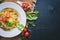 Pasta with bacon, cherry tomatoes, olives, and mushrooms with parmesan cheese. Italian food. On a black wooden surface.