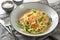 Pasta dish from spaghetti, zucchini, spring onions and prawns in a grey plate on a napkin with parmesan bowl and cutlery,