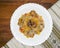 Pasta farfalle with stewed baby octopus and cheese served on a white plate on a wooden table with napkin