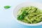 Pasta with green pesto sauce decorated basil leaves and cheese in white plate. Empty space for recipe.