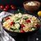 Pasta salad with cucumber, tomato and feta cheese in a bowl on a dark background.