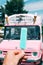 Pastel blue ice cream with a pink ice cream truck or van in the background. Hand holding ice cream.