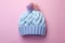 Pastel blue knitted hat with bobble on pink background