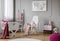 Pastel pink blanket on white rocking chair in spacious baby room interior with cradle, scandinavian ladder and nightstand