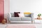 Pastel pink and burgundy pillows on grey sofa in elegant scandinavian living room with red, pink and white wall with copy space