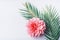 Pastel pink flower and tropical palm leaves on white desktop background, top view, creative layout with copy space