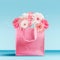 Pastel pink shopping bag with gerbera daisies flowers bunch standing on table at turquoise blue wall background. Branding mock up