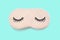 Pastel pink sleep mask with closed eyes embroidered on it with eyelashes on turquoise background. Top view, flat lay.