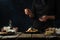 Pastry chef decorates with cinnamon hot waffle on rustic wooden table with ingredients on dark blue background. Backstage of