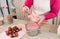 A pastry chef dips strawberries on a wooden skewer into a container with pink chocolate. Preparation of desserts