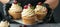 Pastry chef s hands in black gloves decorating cupcakes with cream cheese frosting and red berries