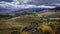 Patagonian landscape of huge hills covered with shrubs, rocks, some trees and a sky full of clouds.