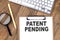PATENT PENDING text on paper clipboard with magnifier and keyboard on wooden background